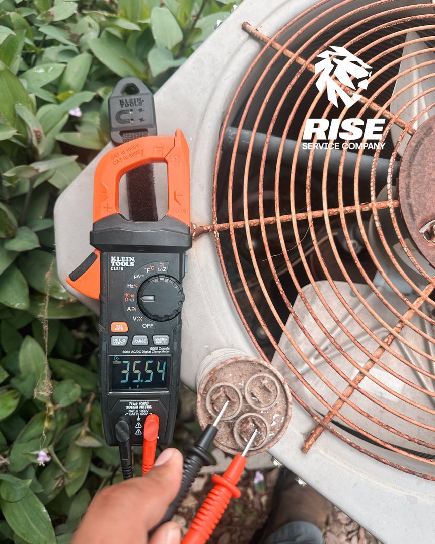 Rise technician testing a capacitor on an outdoor AC unit with a clamp meter
