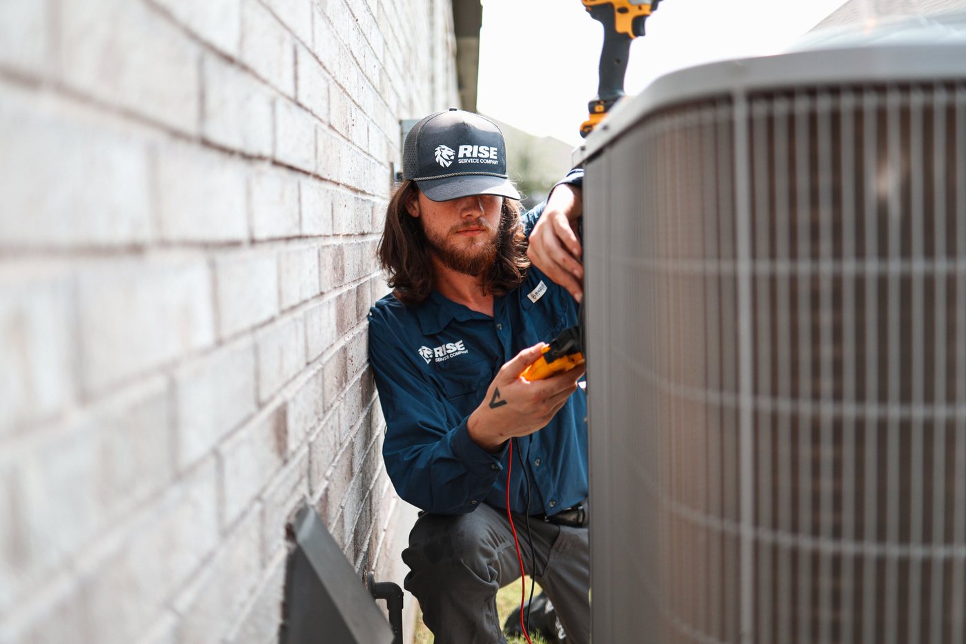 Rise technician checking readings with a meter at an outdoor AC condenser