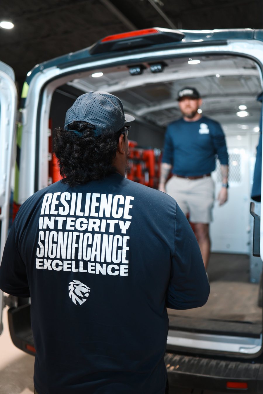 Back of a Rise shirt reading Resilience, Integrity, Significance, Excellence next to a Rise van